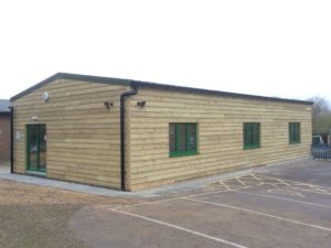 Wood clad school sports hall with forest green coloured windows & doors